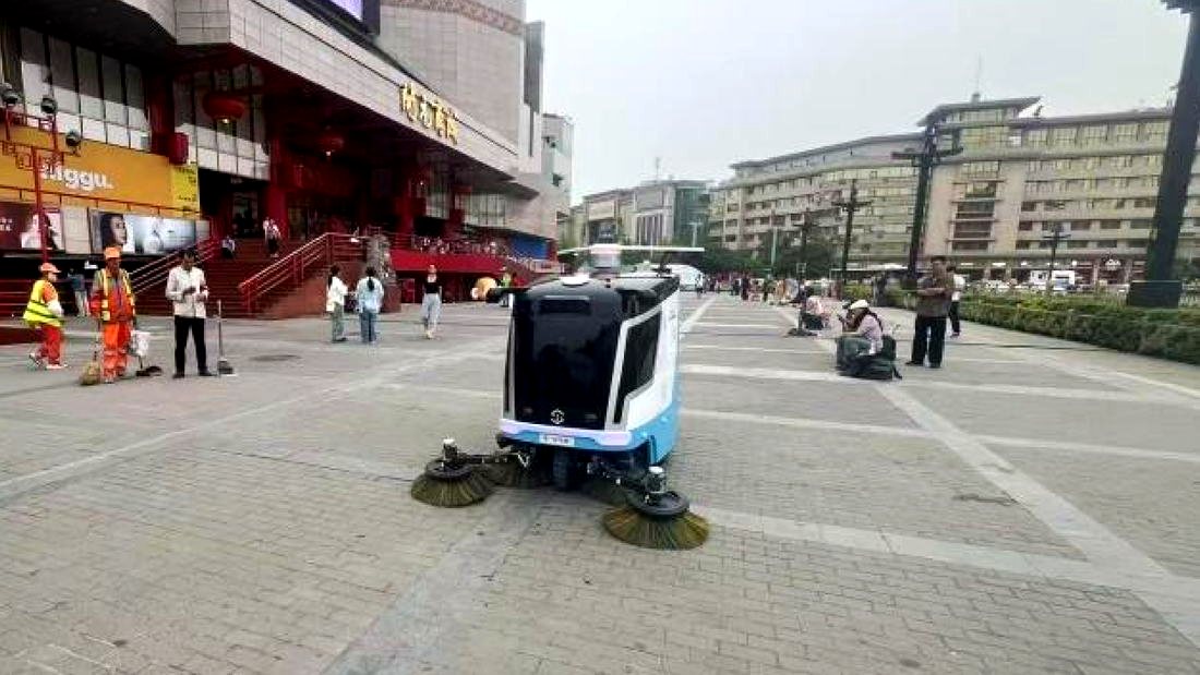 西安钟楼商圈开元商城广场，无人驾驶清扫车正在作业，旁边有环卫工人